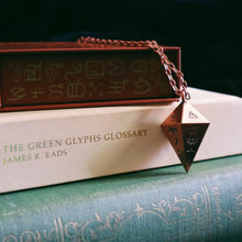 books and a copper pendulum with glyphs