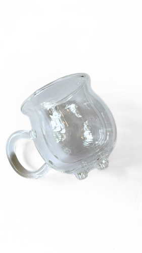 A glass cauldron-shaped mug, featuring a rounded design and a sturdy handle, perfect for serving beverages with a magical touch