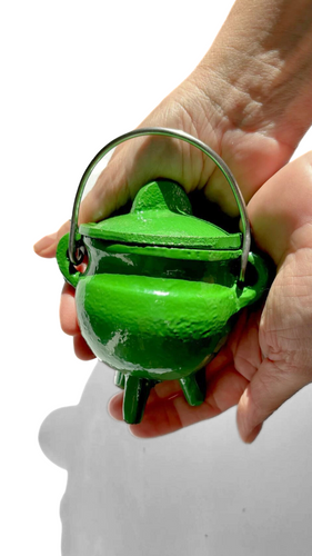 Hands holding a slime green mini cast iron cauldron